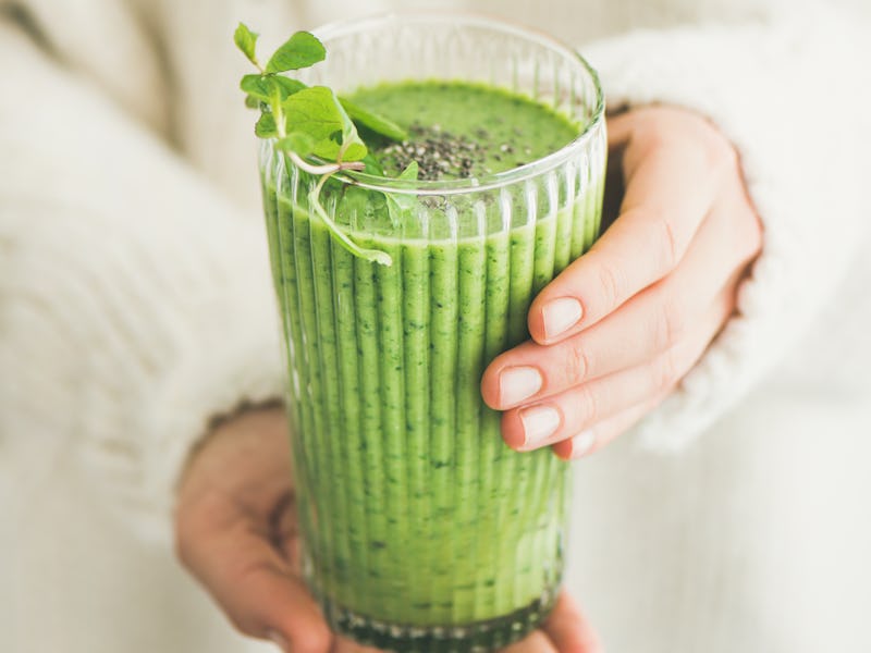 Matcha green vegan smoothie with chia seeds and mint in glass in hands of female wearing white sweat...