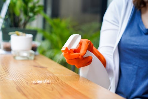 A woman in gloves is cleaning the countertop using a spray spray on the object first to kill germs.