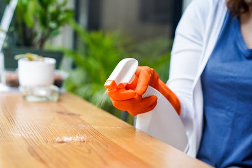 A woman in gloves is cleaning the countertop using a spray spray on the object first to kill germs.