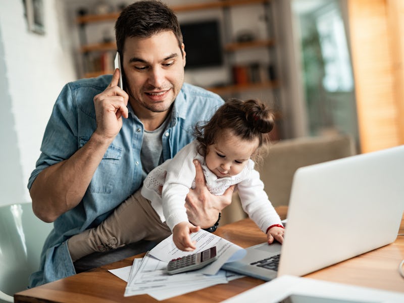 Young working father talking on the phone while babysitting his playful daughter at home.