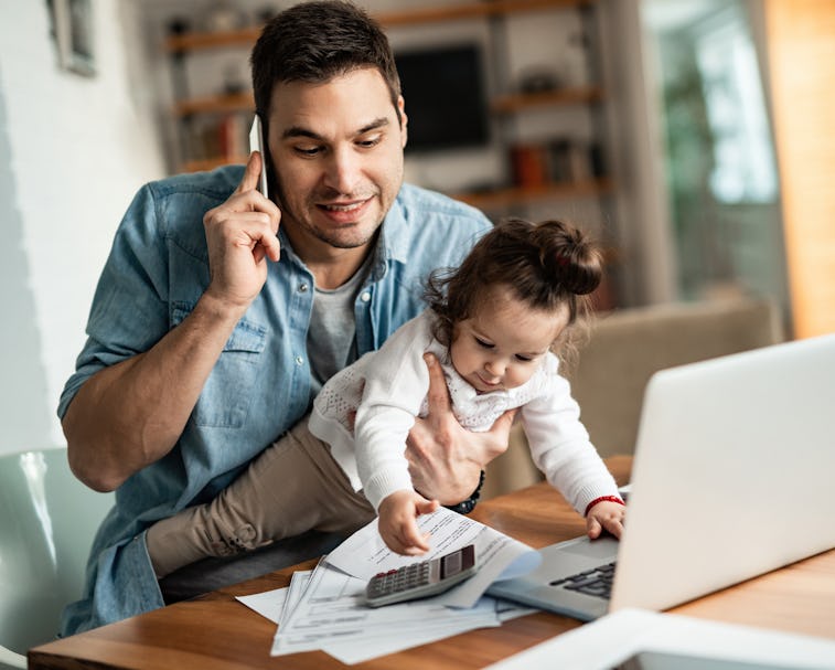 Young working father talking on the phone while babysitting his playful daughter at home.