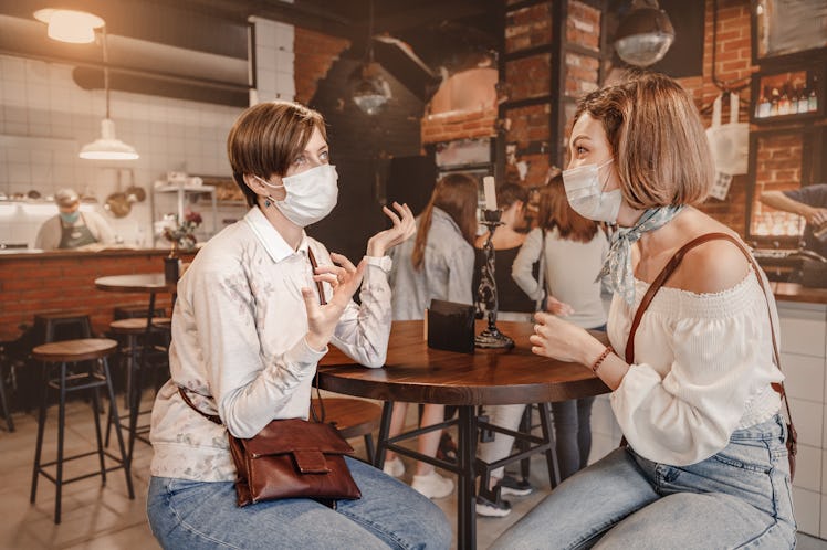 Friends girls met in a cafe and communicate with each other and chat. Wear medical protective masks....