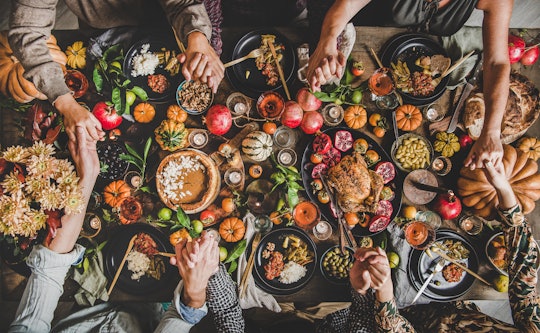 Family praying holding hands at Thanksgiving table. Flat-lay of feasting peoples hands over Friendsg...