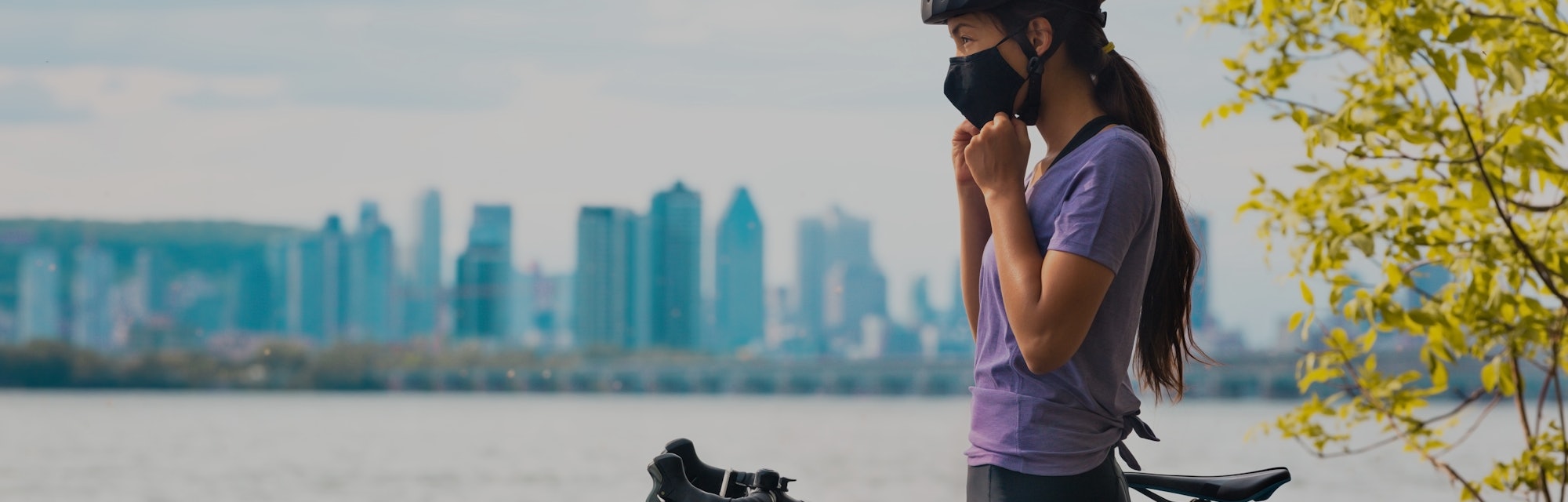 Wearing covid-19 mask while riding bike. Sport cyclist woman biking putting on face mask for Covid-1...