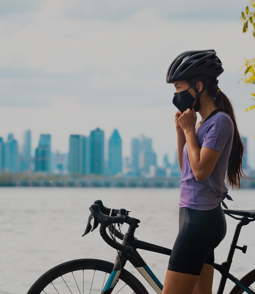 Wearing covid-19 mask while riding bike. Sport cyclist woman biking putting on face mask for Covid-1...