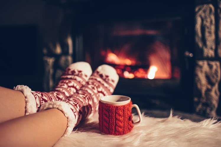 Feet in woollen socks by the Christmas fireplace. Woman relaxes by warm fire with a cup of hot drink...