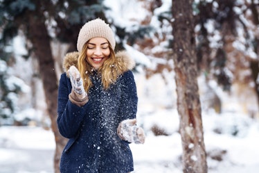Beautiful girl playing with snow in winter forest. Smiling girl in a blue jacket and knitted hat and...