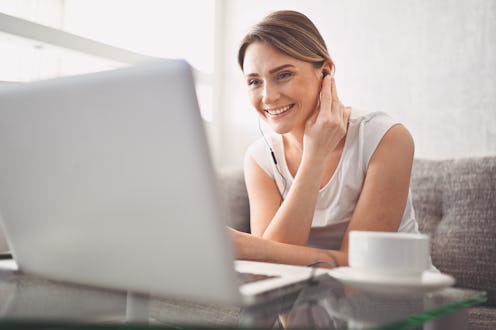 Attractive happy young student studying online at home, using laptop computer, headphones, having vi...