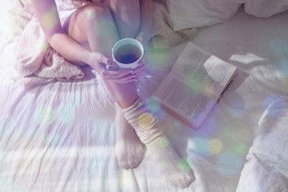Closeup Beautiful Girl in warm knitted Morning Socks. Woman Reading Book and Drinking a Drink in the...