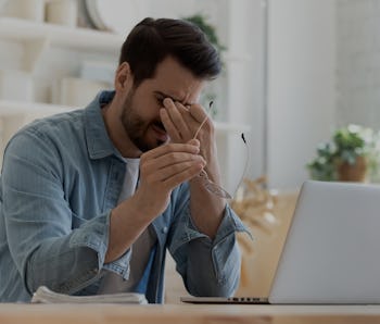 Tired young man feel pain eyestrain holding glasses rubbing dry irritated eyes fatigued from compute...