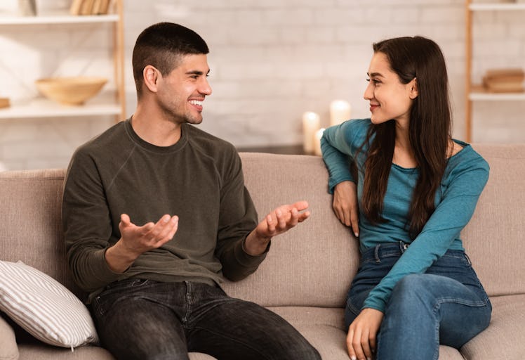 Beautiful couple talking, sitting on couch at home, have a nice conversation at their cozy apartment