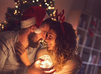 Beautiful couple in love sitting on the living room floor next to a Christmas tree, holding a jar wi...
