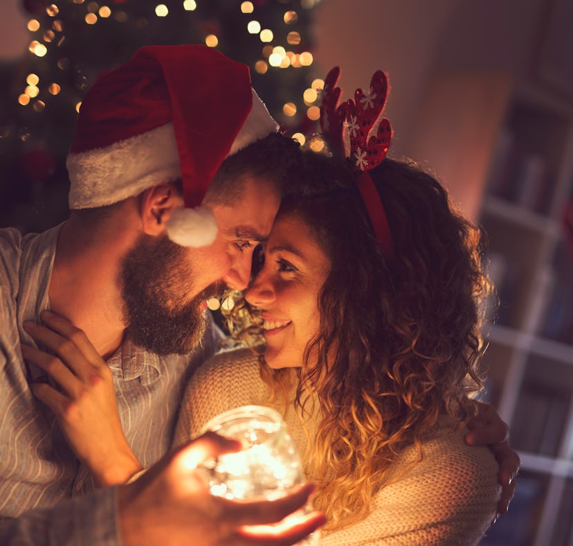 Beautiful couple in love sitting on the living room floor next to a Christmas tree, holding a jar wi...