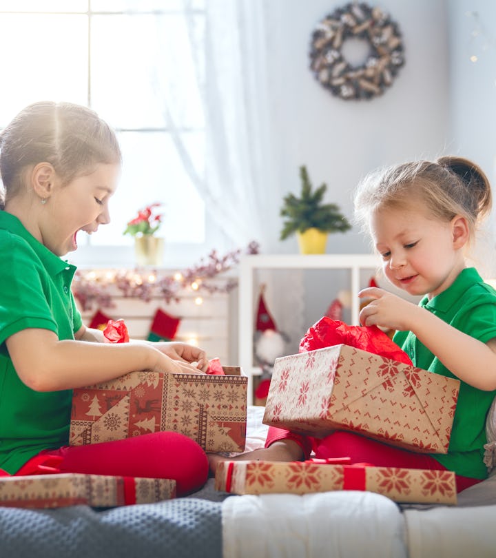 Merry Christmas and Happy Holidays! Cheerful cute childrens girls opening gifts on the bed. Kids wearing pajamas having fun near tree in the morning. Loving family with presents in room.