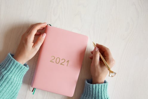 Top view of woman hands in warm sweater with coral coloured 2021 diary book on table. Future plans a...