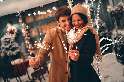 Young romantic couple having fun outdoors in winter before Christmas with sparklers in hands.Enjoyin...