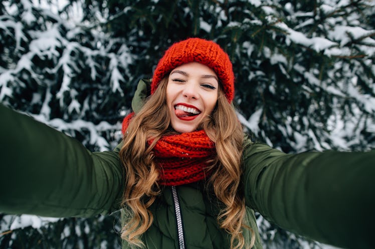 Winter selfie. Young happy girl in red knitted hat and scarf takes selfie and play the ape in winter...