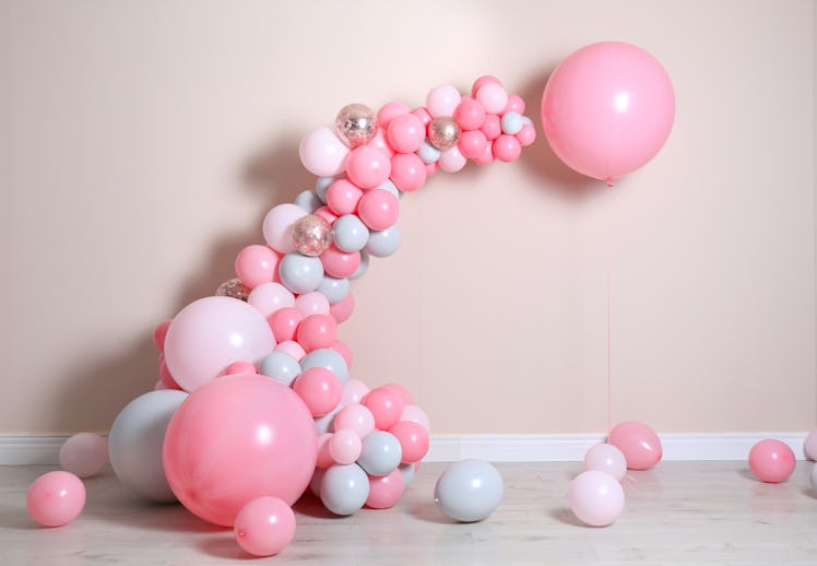 A pink and white balloon arch sits against a beige wall. 