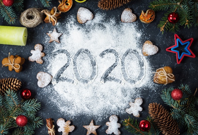 Happy New Year 2020 written on flour and Christmas Decorations Gingerbread cookies on dark stone bac...