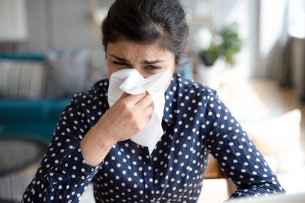 Ill upset indian girl holding paper tissue blowing running nose sneezing in handkerchief got flu fev...