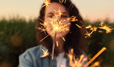 A young woman holds a sparkler in her hands, selective focus. Celebrates the holiday outside, new ye...