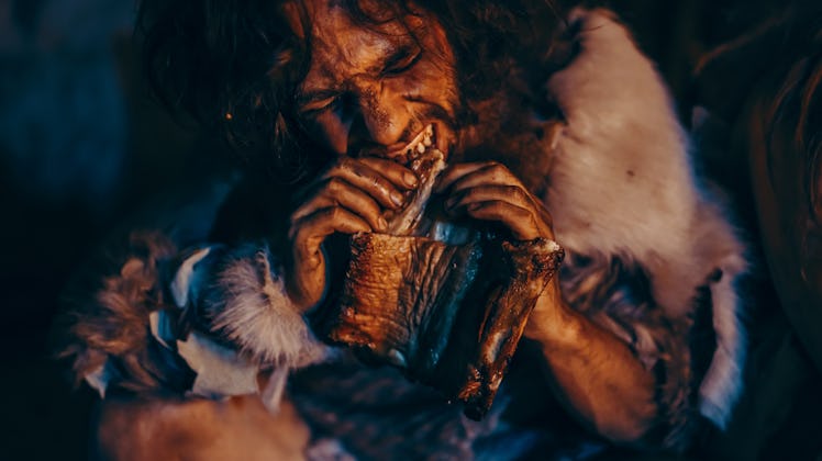 Close-up Portrait of Tribe Leader Wearing Animal Skin Eating in a Dark Scary Cave at Night. Neandert...