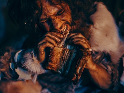 Close-up Portrait of Tribe Leader Wearing Animal Skin Eating in a Dark Scary Cave at Night. Neandert...