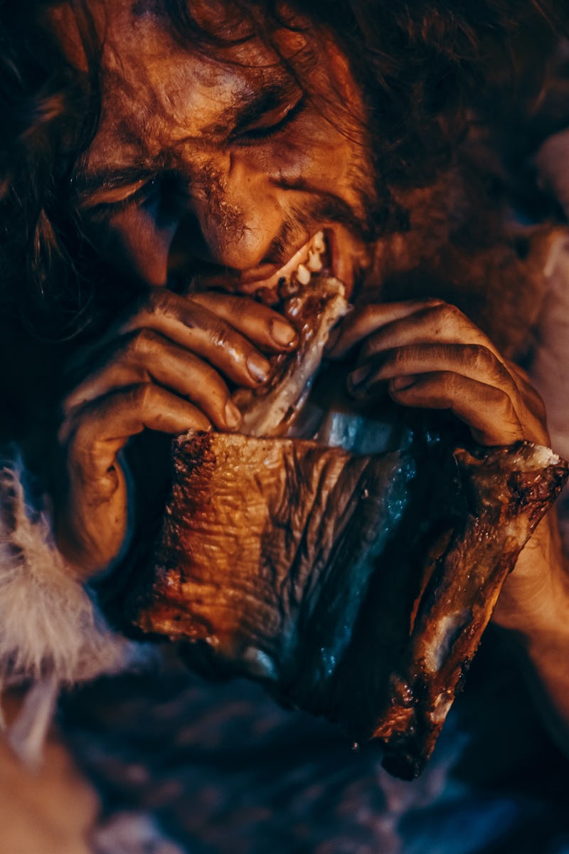 Close-up Portrait of Tribe Leader Wearing Animal Skin Eating in a Dark Scary Cave at Night. Neandert...