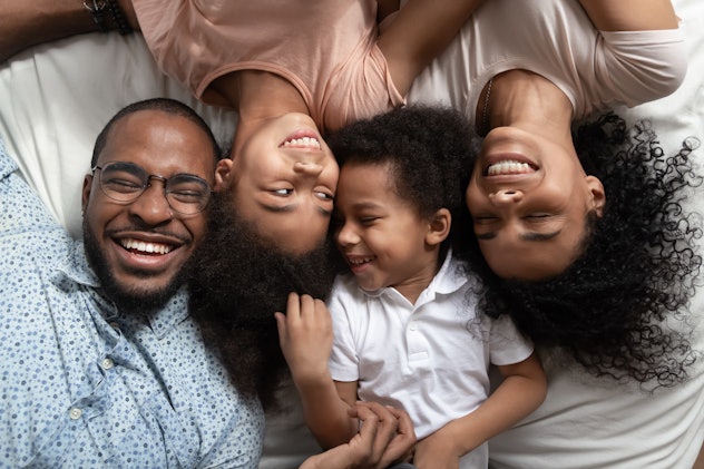 Smiling african american family of four lying on bed head to head with closed eyes, happy parents re...
