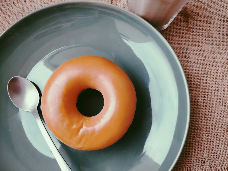 Plain brown doughnut and silver spoon placed on green plate that has a luster.