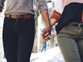 Crop anonymous young multiracial romantic couple in casual clothes holding hands while walking on ci...
