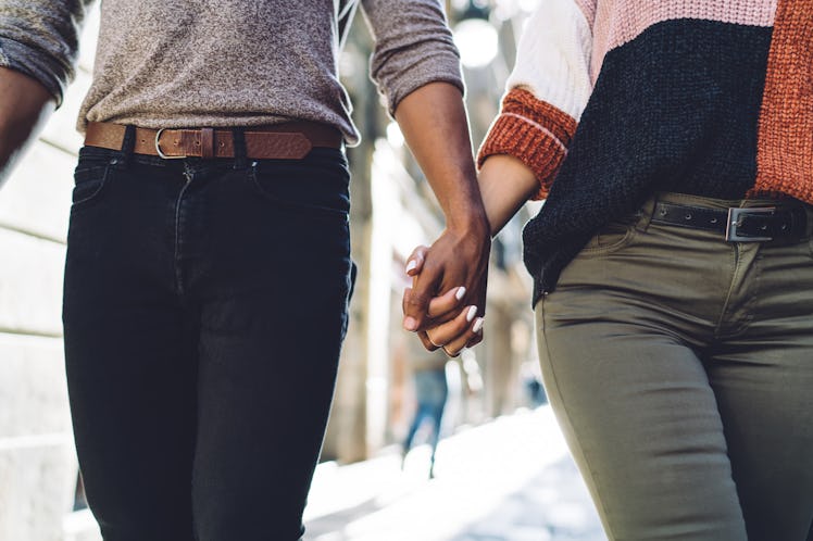 Crop anonymous young multiracial romantic couple in casual clothes holding hands while walking on ci...