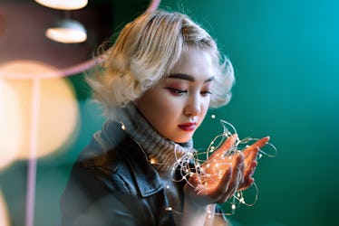 Young adult blonde female asian holding string of fairy lights with bokeh around, selective focus