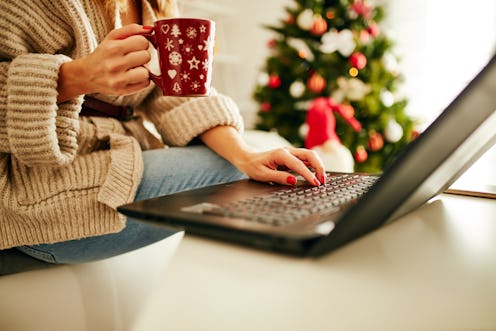 Woman holding cup of coffee while working on laptop at home for Christmas. New Year and Xmas concept...