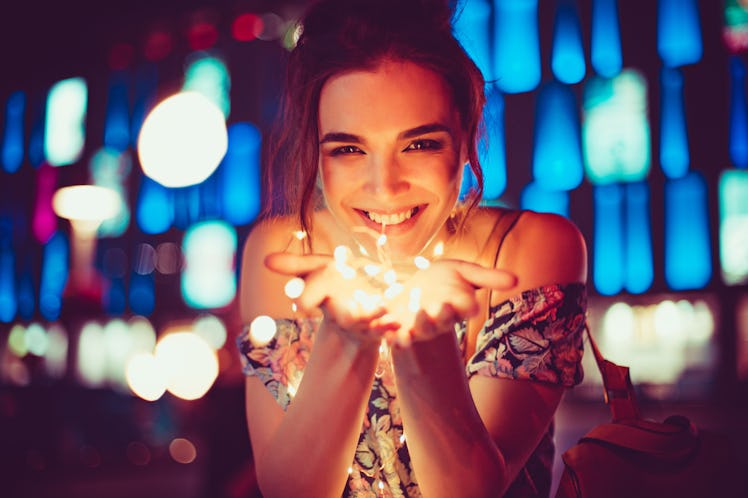 Beautiful young woman smiling and talking garlands of lights at city street
