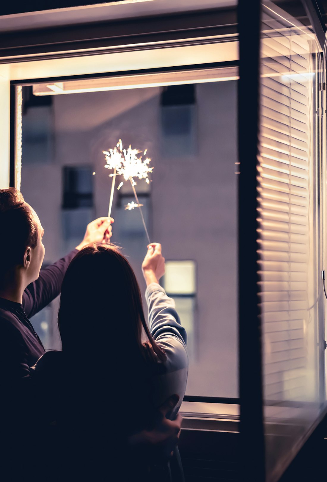 Couple holding sparklers out of the window at night. New year's eve celebration, anniversary, party ...