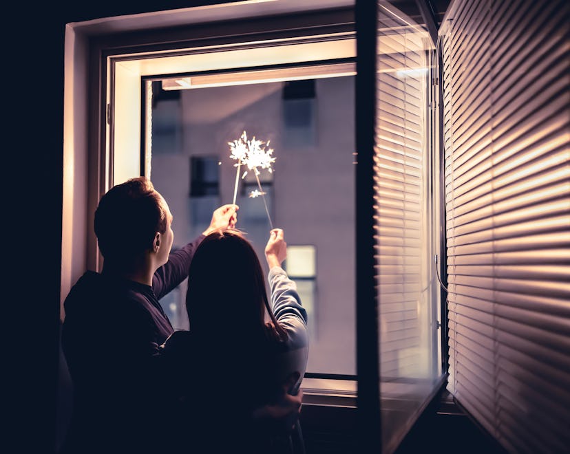 Couple holding sparklers out of the window at night. New year's eve celebration, anniversary, party ...