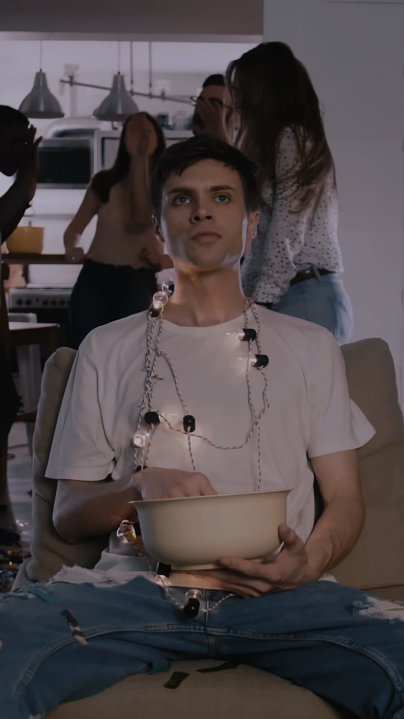 Camera zooms in on young Caucasian man addicted to movies, happy dancing party crowd in the backgrou...