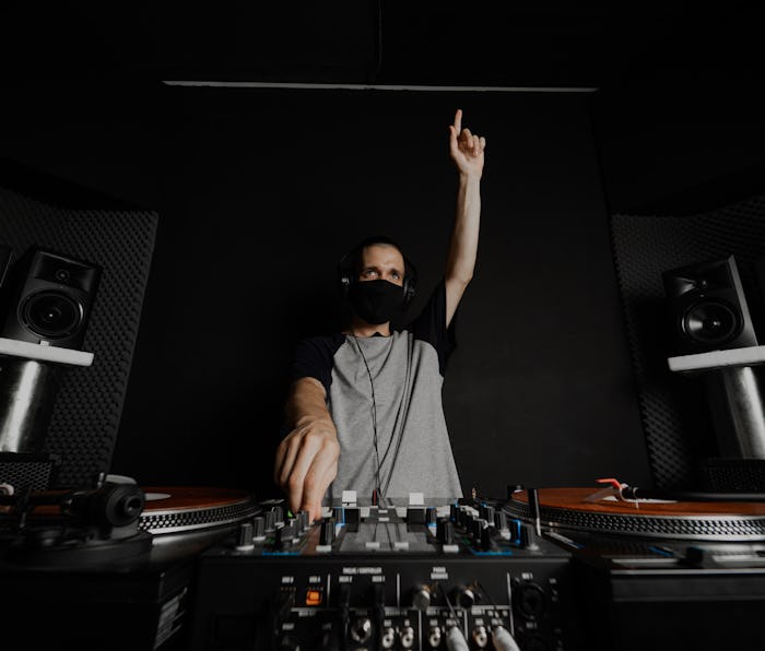 Professional DJ with reusable cloth face mask playing music raising his hand to cheer up the clients...
