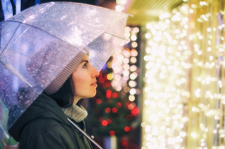 Portrait of young beautiful girl holding umbrella with garland. Posing in Christmas fair, in street ...