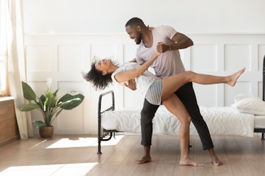 Cheerful active romantic african american couple wearing pajamas dancing in bedroom together, happy ...
