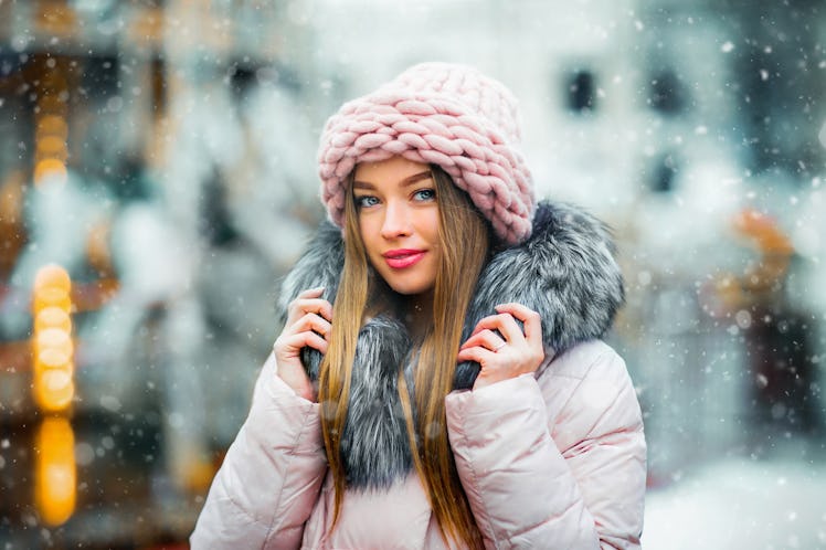 Portrait of a beautiful young model in pink knitted hat standing near carousel on a christmas backgr...