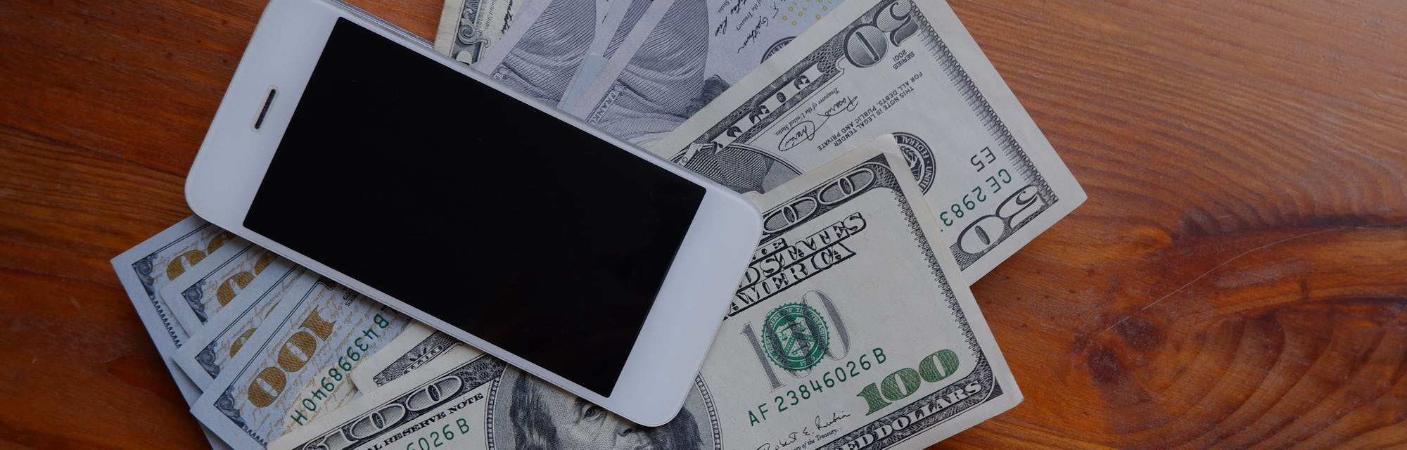 Mobile phone and money on a wooden background. The concept of making money using a smartphone. Pile ...