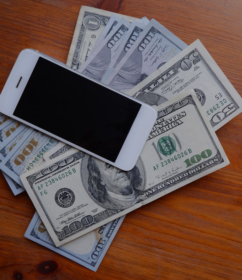 Mobile phone and money on a wooden background. The concept of making money using a smartphone. Pile ...