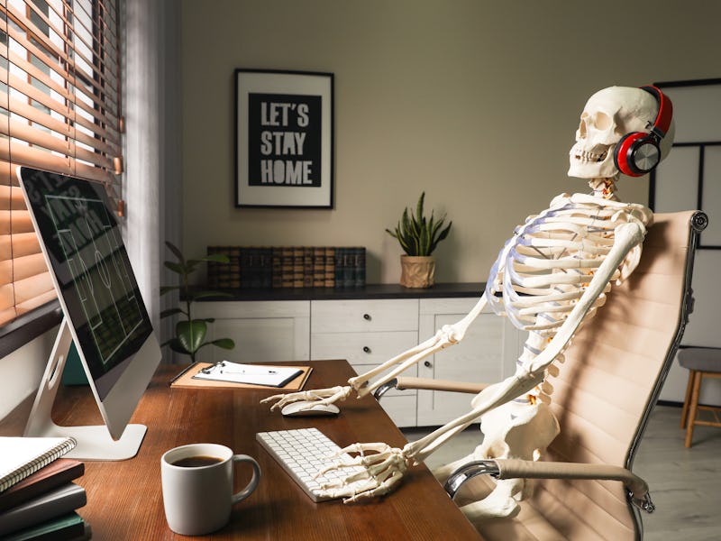 Human skeleton with headphones using computer at workplace