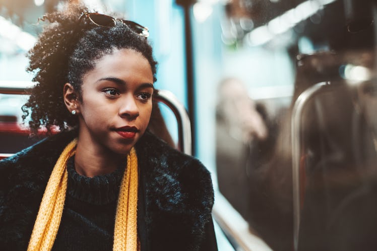 A cute young African-American female on a seat of metro in a demi-season coat and yellow scarf is th...