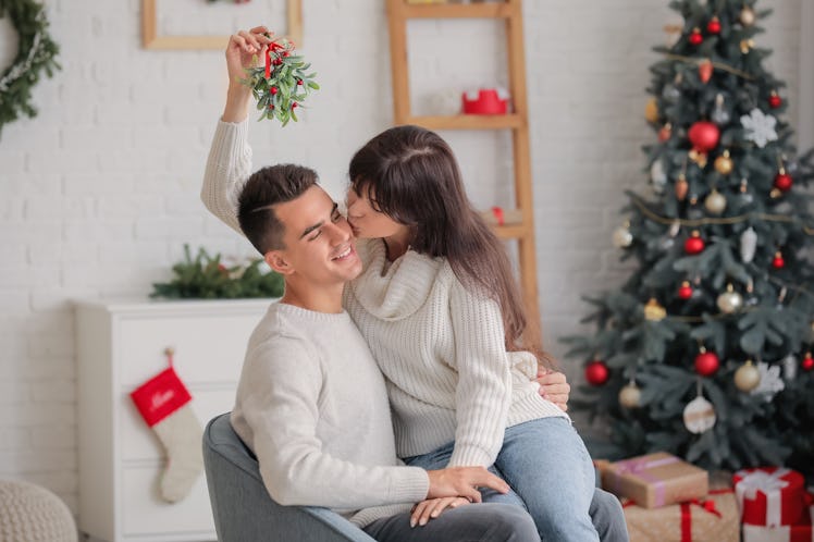 Young woman kissing her husband under mistletoe branch at home on Christmas eve