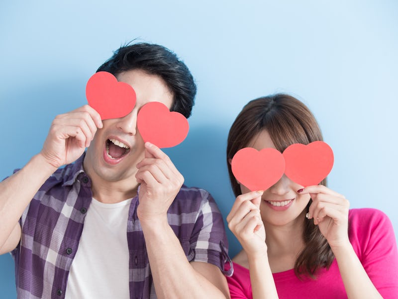 Attractive young couple holding red love hearts over eyes isolated on blue background