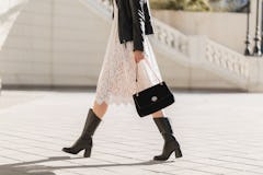 legs of attractive woman walking in street in high leather boots, fashionable outfit, holding purse,...