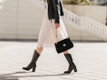 legs of attractive woman walking in street in high leather boots, fashionable outfit, holding purse,...